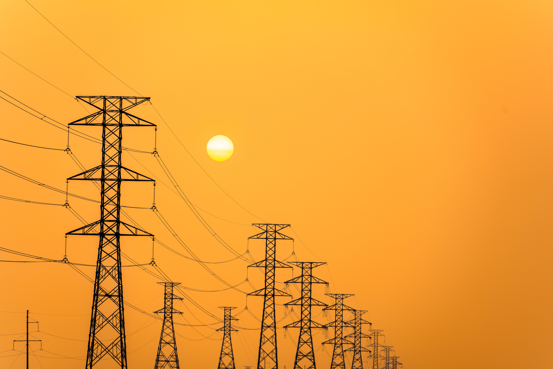 High-voltage transmission towers and power lines silhouetted against an orange sunset sky