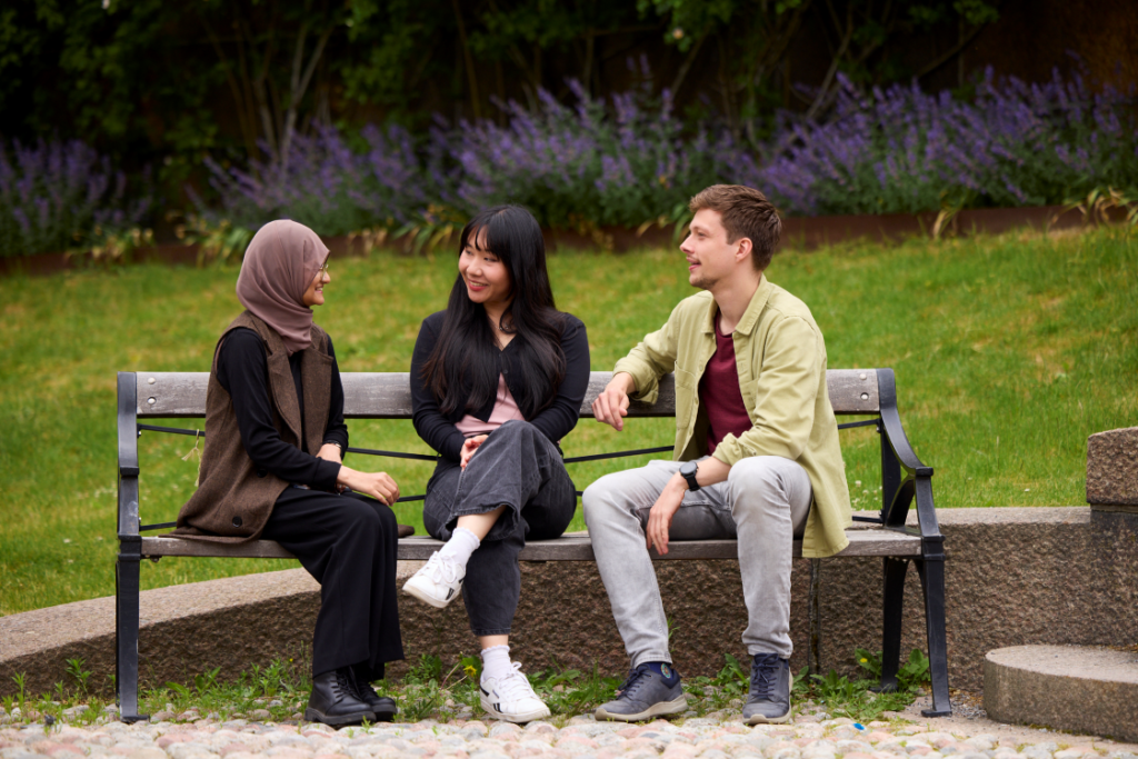 Three Masters+ students talking together on a bench outdoors
